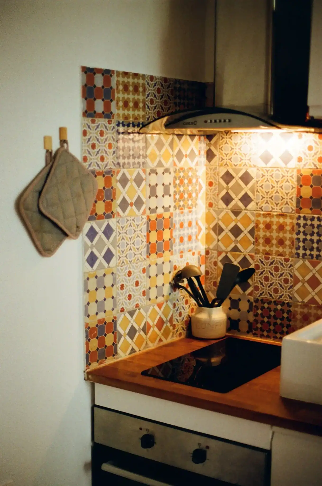 Warm kitchen corner with colorful Moroccan patchwork tile backsplash above induction cooktop