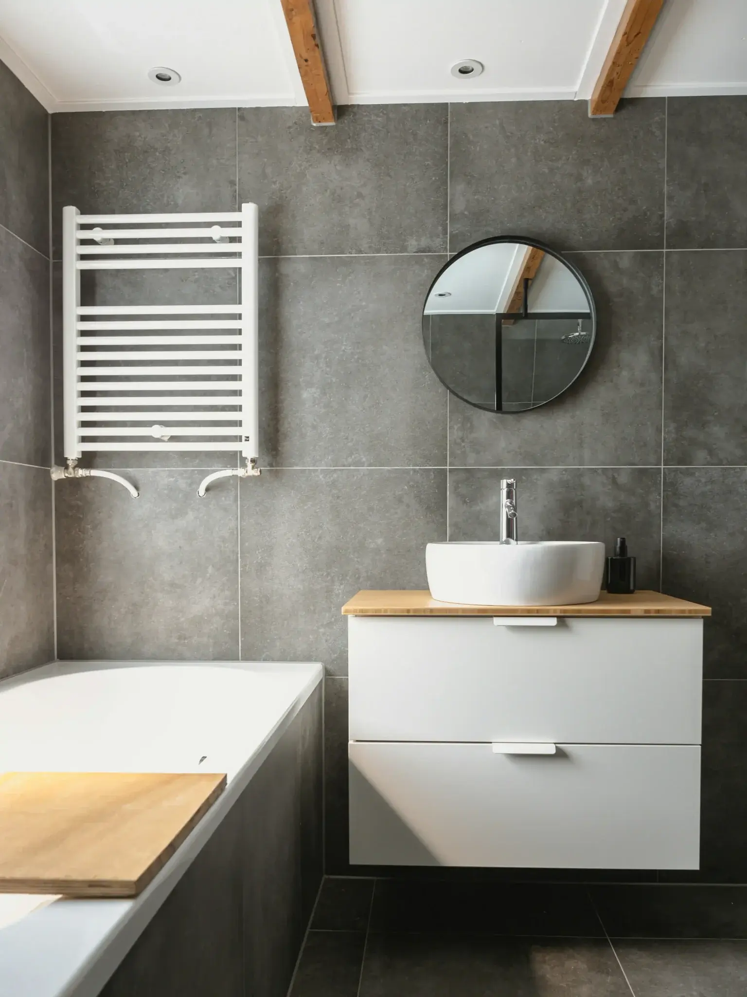 Dark slate tile bathroom with floating vanity, round mirror, and exposed wood ceiling beams