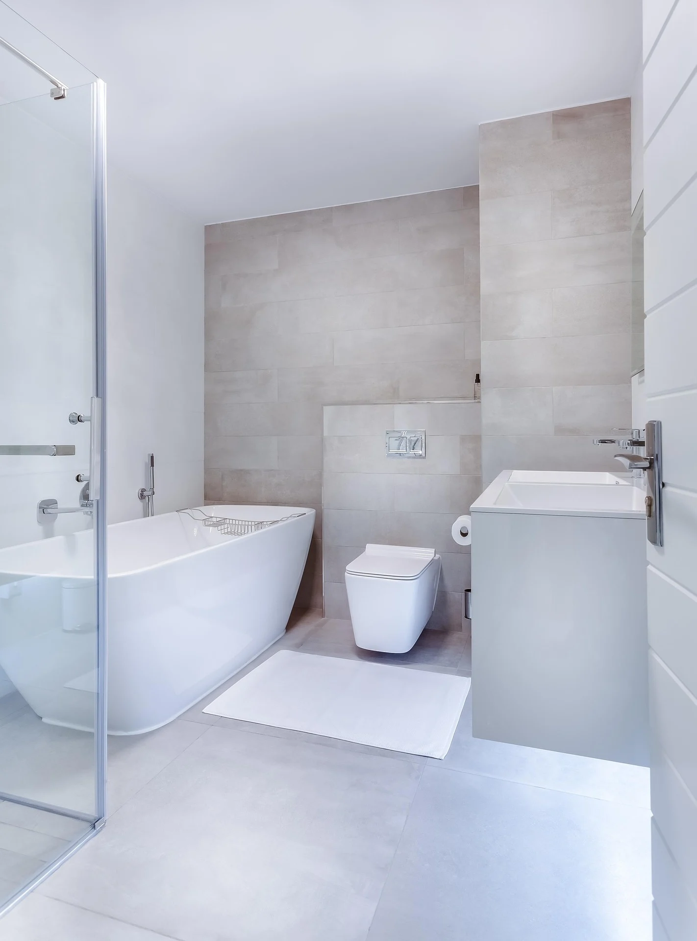 Modern white bathroom with freestanding tub, wall-hung toilet, and large-format beige tile