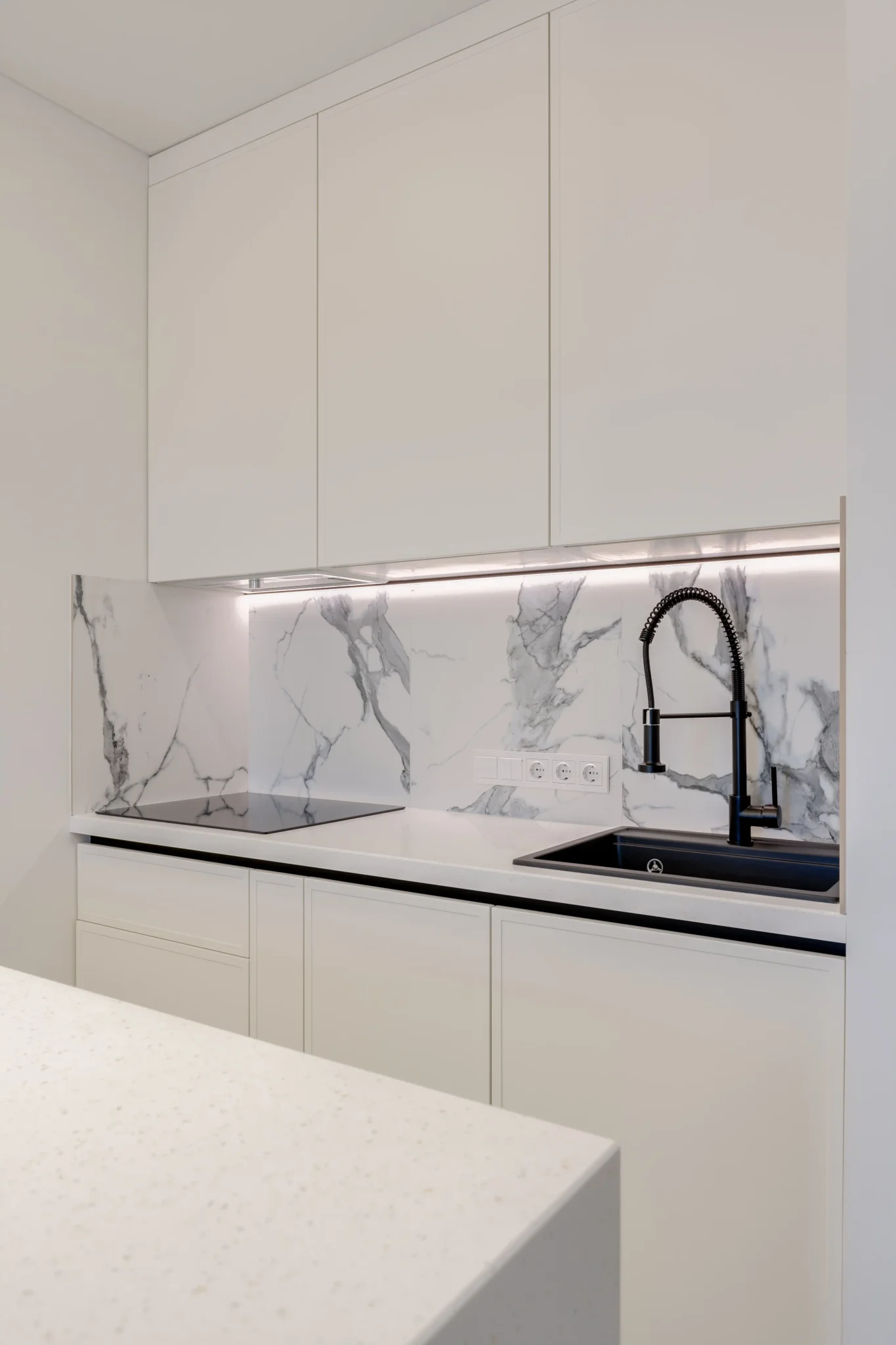 Minimalist white kitchen with large-format marble tile backsplash and matte black pull-down faucet